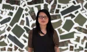 The artist standing in front of a background with green asymmetrical shapes