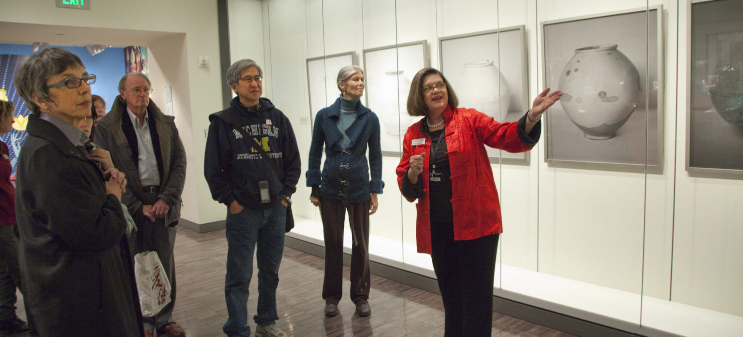 A docent wearing a red jacket speaks to a group of visitors