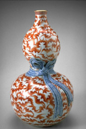 A vase in the shape of a gourd with a blue ribbon around the middle