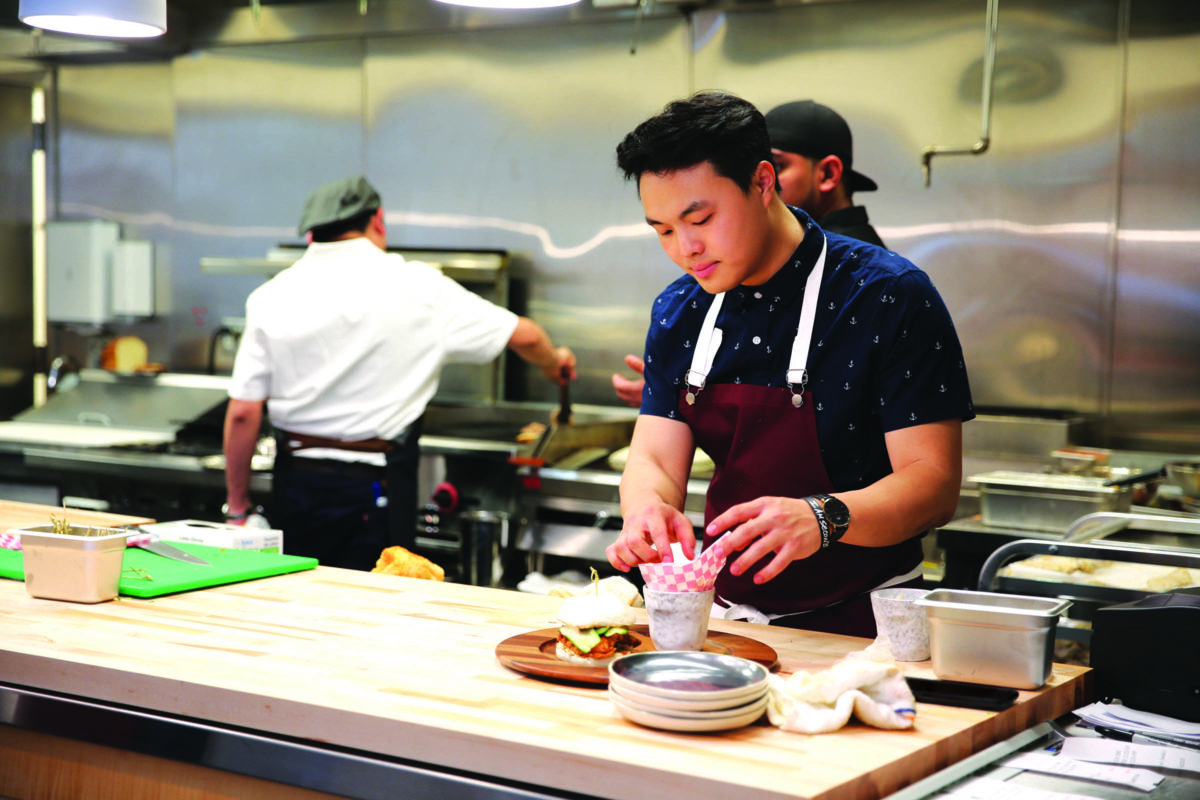 A man wearing an apron composes a plate of food.