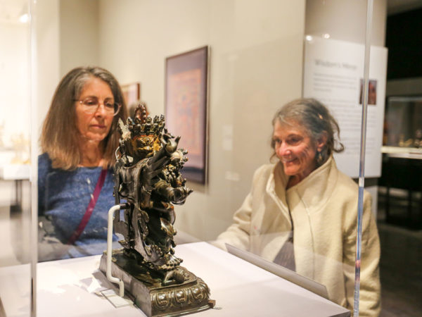 Two women look at a small sculpture in a glass case.