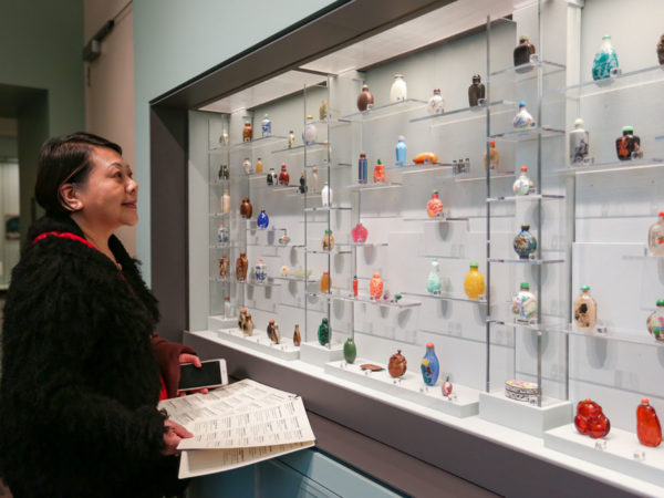 A woman looks at a large collection of snuff bottles in a glass case.