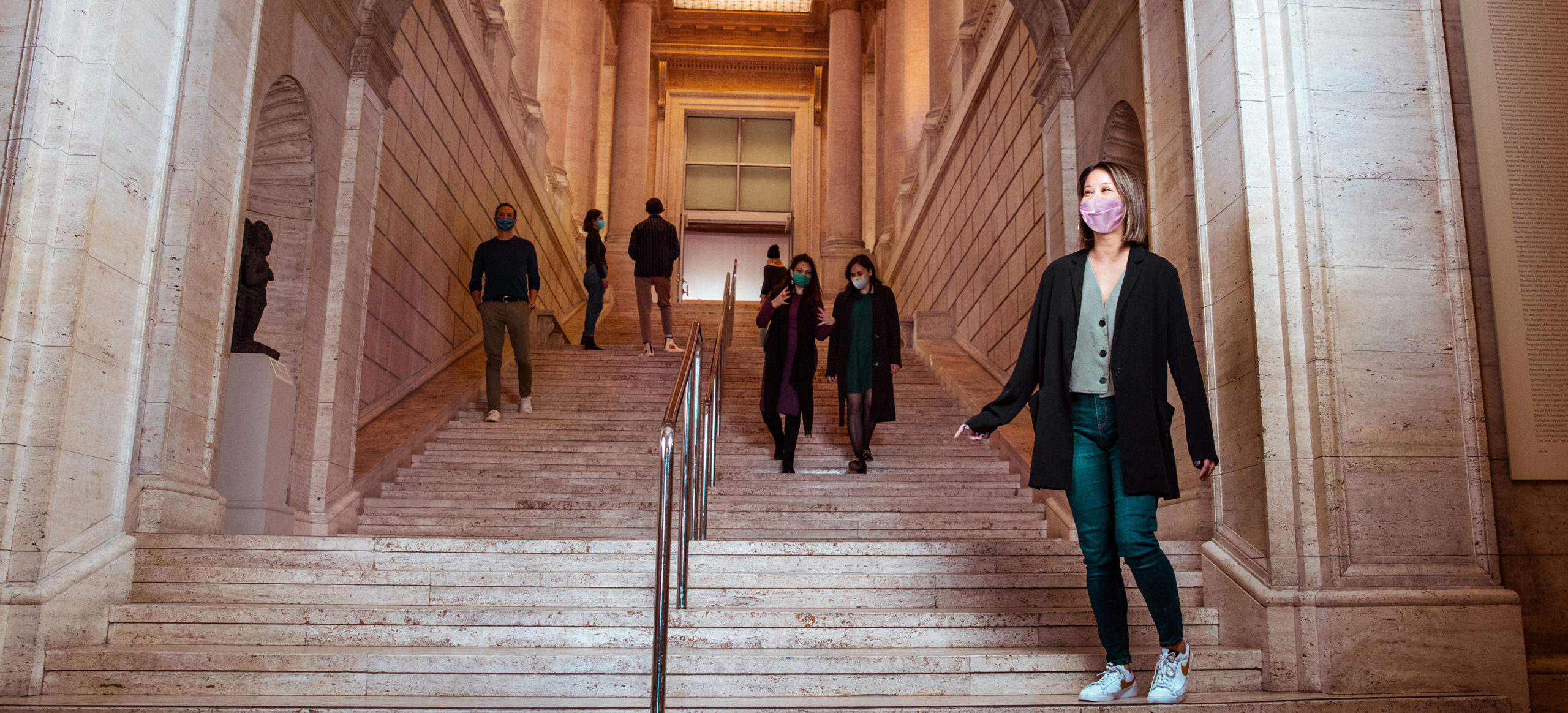 A woman wearing a mask descends a grand staircase.