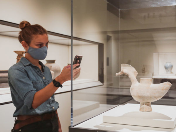 Woman reads information on cell phone while standing in front of a vessel shaped like a duck.